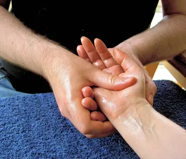 therapist performing professional hand massage therapy with oil, focusing on palm and finger techniques for hand and wrist relief