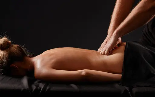 therapist providing professional lower back massage to female client lying face-down on table. hands apply targeted pressure to lumbar region for lower back soothing relief
