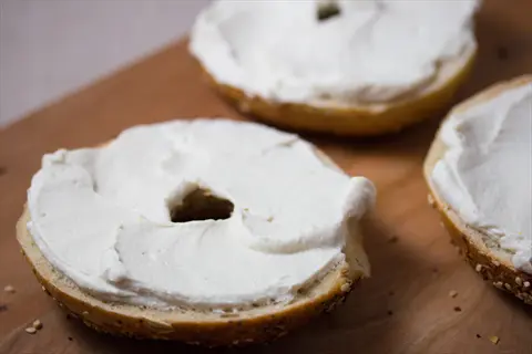 three bagel halves with creamy cashew cream cheese spread, displayed on a wooden cutting board