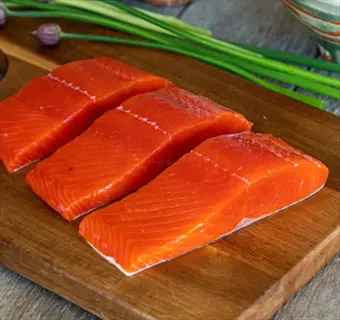 three fresh salmon fillets on a wooden cutting board with green onions - a healthy, fatty fish choice