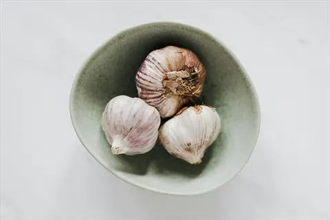 three garlic bulbs in a light green ceramic bowl on a marble table