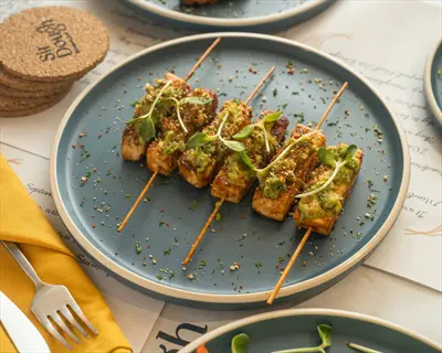 tofu vegetable skewers with green avocado topping and sprouts on blue plate, background with restaurant menu text