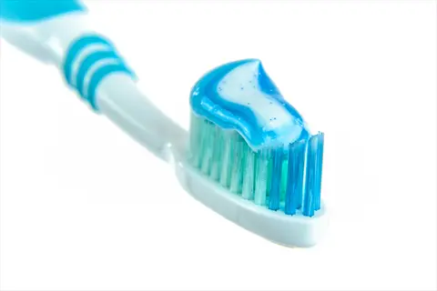toothbrush with blue-and-white striped toothpaste showing creamy texture on bristles against white background