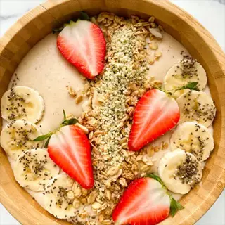 top-down view of oatmeal bowl with fresh strawberries, banana slices, granola, chia seeds, and hemp seeds - complex carbohydrates source