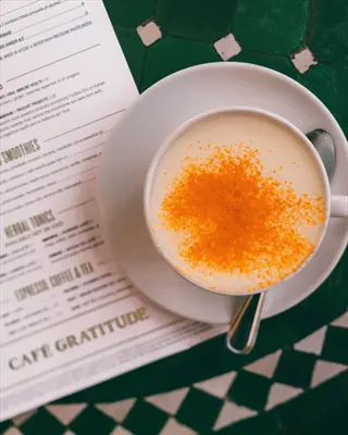 turmeric-spiced beverage in white cup at café gratitude, supporting turmeric metabolism benefits, with menu on green mosaic-tiled table