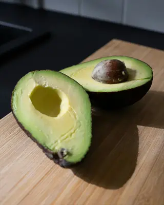 two avocado halves (sliced) with pit visible in one half, on a wooden cutting board