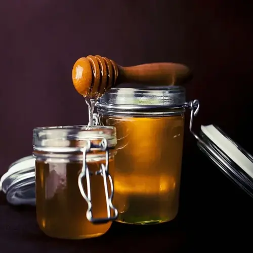 two glass jars of manuka honey with a wooden honey dipper dripping syrup
