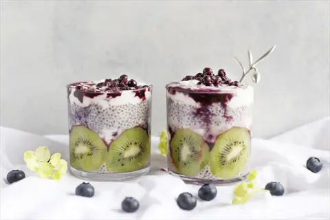 two glasses of chia yogurt topped with mixed berries and kiwi slices, a vibrant breakfast boost with fresh blueberries scattered around
