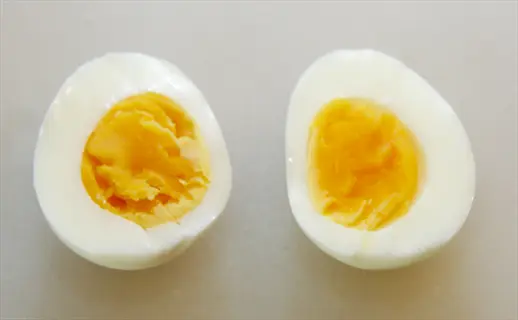 two halves of a boiled egg (sliced) on a light surface, showing runny yolks - embodies 'boiled eggs sliced' and 'eggs'