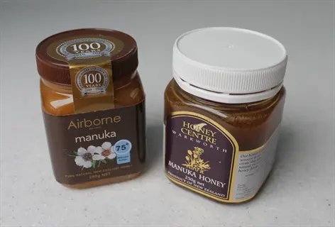 two manuka honey jars showcasing product labels: 'airborne' (brown label with floral graphic) and 'honey centre' (purple label), implying creamy texture