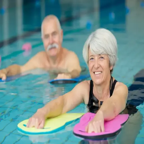 two older adults smiling during aquatic therapy pool exercise with flotation boards