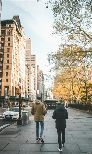 two people city street walking on an urban sidewalk with tall buildings, autumn trees, and a police car