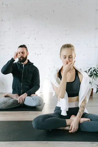 two people practicing counting breaths meditation with alternate nostril breathing in a white brick studio, seated on yoga mats