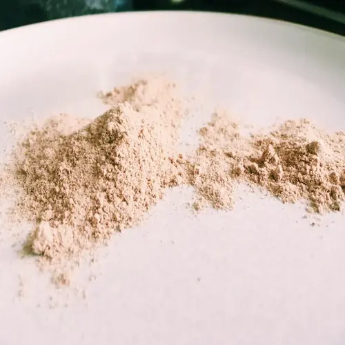 two piles of psyllium husk powder on a white plate with dark background