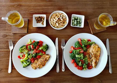 two small portion plates with grilled chicken, broccoli, cherry tomatoes, nuts, and snacks arranged for portion control on a wooden table