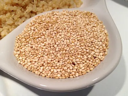 uncooked quinoa seeds with visible grains in white ceramic dish, background features cooked quinoa