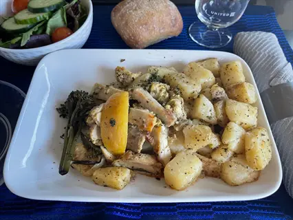 united airlines meal featuring lemon balm chicken with roasted potatoes, lemon slice, and seasonal vegetables