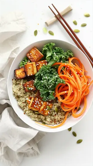 vegan tofu quinoa bowl with spiralized carrots, kale, sesame seeds, and pumpkin seeds. served with chopsticks and a wooden rest on a light background
