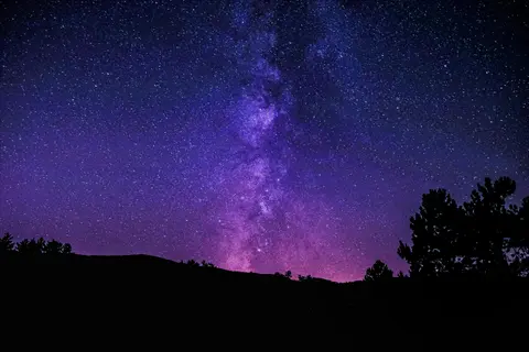 vibrant night sky stars and milky way galaxy over silhouetted trees and hills