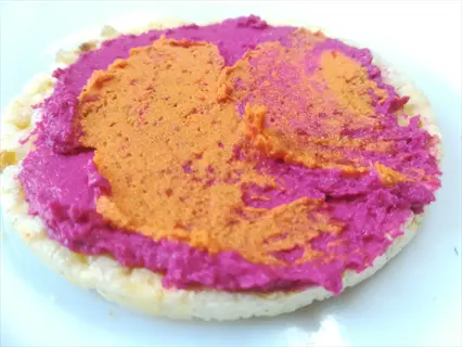 vibrant pink beetroot hummus and orange dip spread on a crisp cracker, served on a white plate