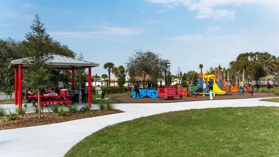 vibrant sensory awareness park featuring red pavilion, colorful playground equipment, paved pathways, and visitors enjoying the sunny outdoor space