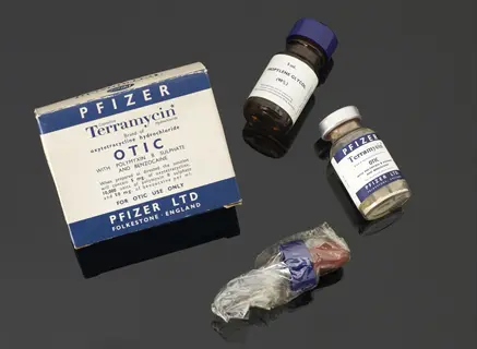 vintage pfizer terramycin antibiotics medicine bottles with blue-and-white labels, box, and dropper on reflective surface - mid-century pharmaceutical design
