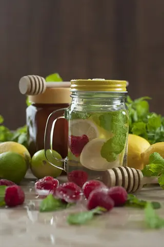 water fruit infusion in a jar with lemon, raspberry, mint, honey dippers, and limes - refreshing hydration choice