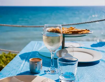 water glass beside meal on a blue tablecloth with ocean view, featuring a wine glass, coffee cup, and toast platter