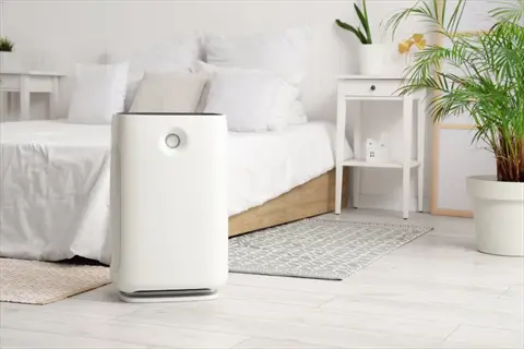 white bedroom air purifier in a modern light-toned bedroom with bed, rugs, and potted plants - air quality improvement