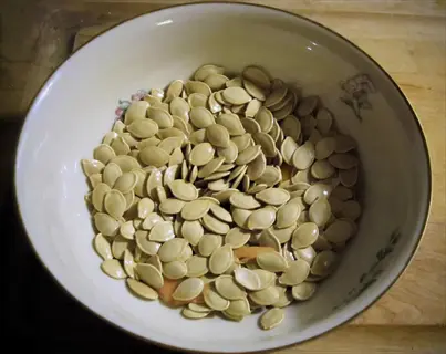 white bowl filled with roasted pumpkin seeds, showing light brown seeds with a glossy texture on a wooden surface