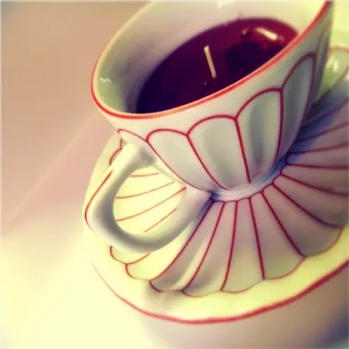 white rooibos tea cup with red scalloped patterns on matching saucer, containing dark liquid and candle wick