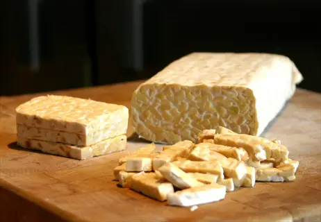whole and sliced tempeh on wooden cutting board, showcasing fermented soybean cake texture