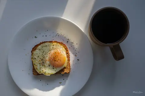 whole grains eggs breakfast: toasted bread with fried egg and coffee in sunlit morning setting