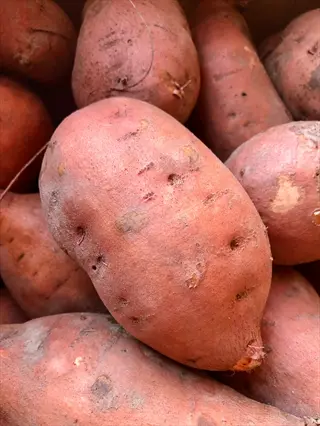 whole sweet potatoes with reddish-brown skins piled together, showing natural texture and imperfections