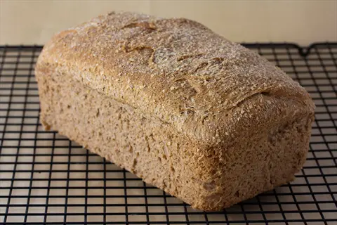whole wheat bread: a freshly baked loaf with golden-brown crust and seeded topping rests on a black wire cooling rack
