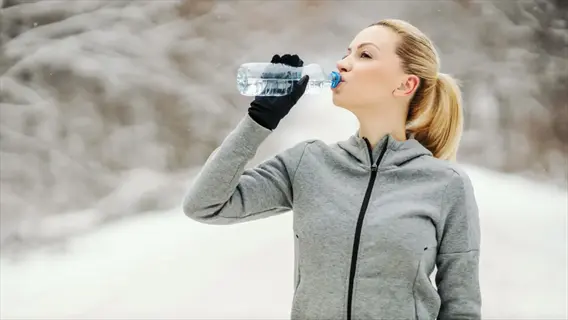 winter athlete drinking water during outdoor workout in snowy forest wearing gray hoodie and black gloves