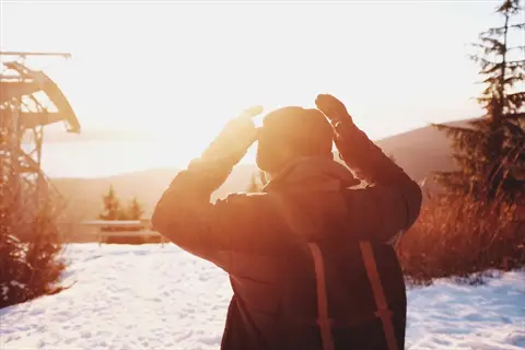 winter sunlight person: hiker adjusting beanie in snowy mountain landscape at sunrise, for seasonal depression prevention through natural light exposure