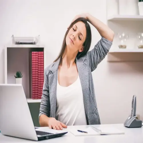 woman doing neck stretch at office desk with laptop and supplies