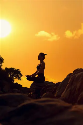 woman meditating at sunrise in lotus position on rocks, serene natural landscape