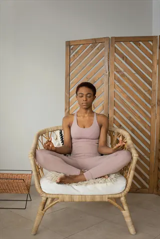 woman meditating in comfortable meditation chair with cushions, seated in serene indoor space with wooden screen and minimal decor
