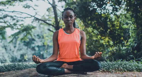 woman meditating in lotus position outdoors among trees - embodying mindfulness mastery