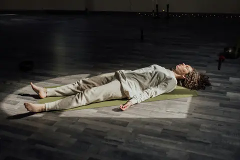 woman meditating lying down in savasana pose on yoga mat with soft lighting, eyes closed