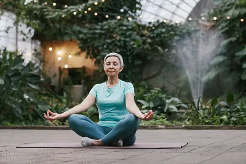 woman meditating outside in garden with string lights and fountain - breathwork techniques
