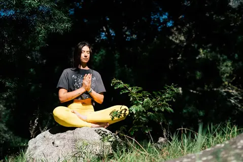 woman practicing mindful breathing meditation in anjali mudra pose seated on a rock in a serene forest setting
