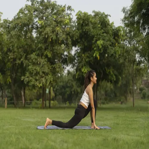 woman practicing yoga on a grassy field in a park during a sunny morning