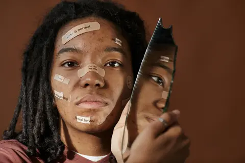 woman with affirmation-written bandages on face holding a mirror - emotional honoring