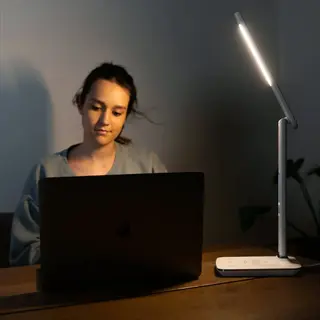 woman working on laptop at night with carex theralite radiance light therapy lamp illuminating the desk (face visible)