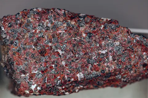 zinc mineral rocks closeup: coarse-grained rock fragment with angular dark gray crystals in reddish-brown matrix and white mineral veins